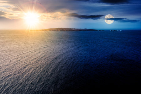 island in the sea at summer solstice. seascape with land in the distance beneath a sky with sun and moon. day and night time change conceptの写真素材