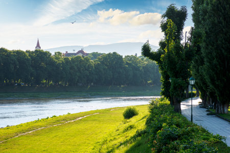 embankment of the river uzh in morning light. historic center of uzhhorod city. wonderful urban landscape in summer. linden alley on the left shoreの写真素材