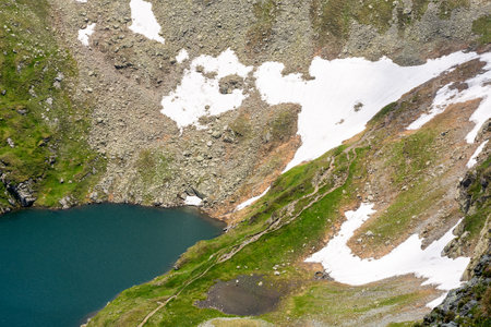 capra lake of fagaras ridge in summer. pristine remote torrent. rippled water surface and grass on the shore view from above. alpine pond carpathian mountains of romaniaの写真素材