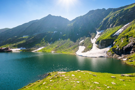 balea lake of romania. alpine landscape of fagaras mountains with pond. sunny weather with clouds on the blue sky above carpathians. snow and grass on the hillside in summer. vacation seasonの写真素材