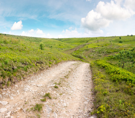 country road through grassy hills. travel destination. scenery in dappled light. scenery of smooth mountain in summer. clouds on the sky. beautiful nature landscapeの写真素材