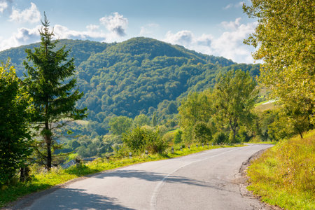 mountain pass on a sunny evening. road winding down the hill. trees on the roadside. forested hill in the distanceの写真素材