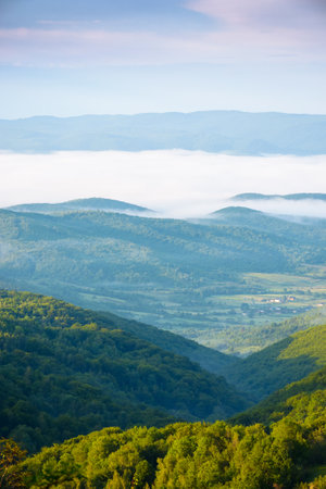 mountainous countryside landscape with fog in the distant valley. mist rolling among hills in morning light. stunning view of carpathians in summer. clouds on the blue sky. amazing daleの写真素材