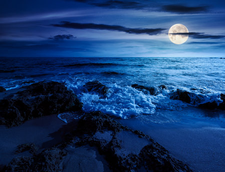 beach with sand at night. summer vacation at the seaside. beautiful seascape with calm waves in full moon light. landscape at the sea under sky with fluffy cloudsの写真素材