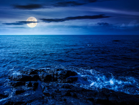 sea coast with rocks and boulders at night. calm summer vacation background at the seashore. wonderful scene for relax and leisure at the seaside in full moon lightの写真素材