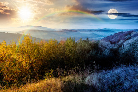 view from a mountain in to the foggy valley. day and night time change concept. beautiful autumn equinox. forested hills with sun and moon at twilight. picturesque alpine countryside sceneryの写真素材