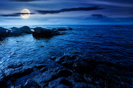 weekend on a rocky beach at the black sea under open dark sky at night. beautiful coastline in summer. seascape scenery with clouds above horizon in full moon light. mysterious weatherの写真素材