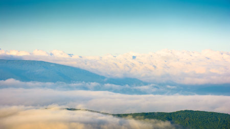 spring mountain landscape with fog in valley and clouds on blue sky in morning light. dramatic atmosphere phenomenon view from the top. evaporating forest on the hillsの写真素材