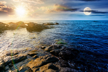 weekend on a rocky beach at the sea. day and night time change concept. beautiful coastline on summer solstice. seascape scenery with clouds above horizon with sun and moon at twilight. mysterious weatherの写真素材