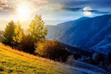 autumn equinox in mountain landscape. day and night time change concept. beautiful view of trees in fall foliage on the hillside with sun and moon at twilight. alps of countryside under dramatic skyの写真素材