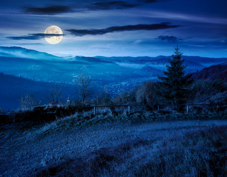view from a mountain in to the foggy valley at night. beautiful autumn landscape. forested hills in full moon light. picturesque alpine countryside sceneryの写真素材