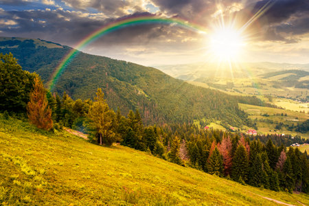 mountain landscape under blue sky with clouds at sunset. countryside scenery with green meadow, rolling hills and valley in evening light. hiking place in summer. storytelling image under the rainbowの写真素材