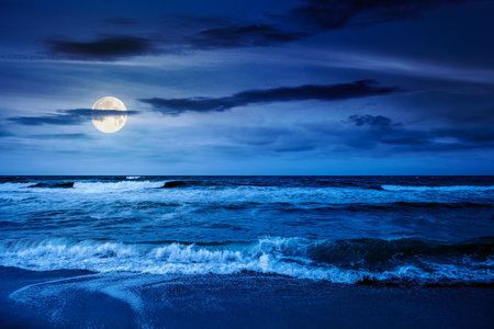 black sea waves crashing sandy beach at night. summer vacation on a windy weather under dark cloudy sky in full moon light. view of dramatic seascape. background for abstract conceptsの写真素材