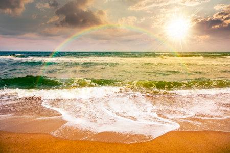 black sea waves crashing sandy beach at sunset. summer vacation on a windy weather under cloudy sky in evening light. view of dramatic seascape. storytelling image under the rainbowの写真素材