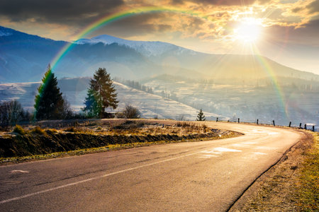 country road in mountains at sunset. beautiful countryside landscape in late autumn. fir trees on the roadside in evening light. scenic view of blue sky with clouds above the distant ridge in snowの写真素材