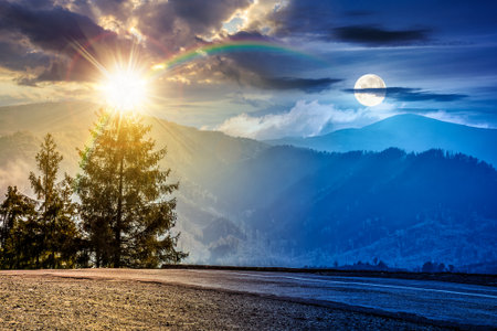 old asphalt road going through the hillside and passes green spruce forest. day and night time change concept. landscape with distant mountains with sun and moon. duality and transition templateの写真素材