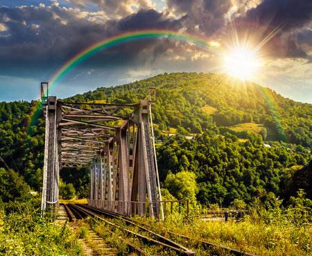 old metal rail road bridge in rural area in mountains at sunset. journey through beautiful landscape in evening light. transportation or retro technology concept. storytelling image under the rainbowの写真素材