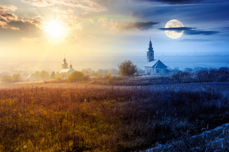 old church in the village in autumn. day and night time change concept. view of countryside landscape from a hill in haze with sun and moon. empty rural fields. duality and transition templateの写真素材