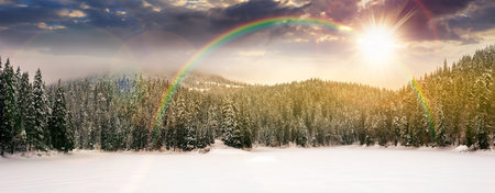 panorama of beautiful mountainous landscape in winter at sunset. spruce forest around the snow covered and frozen lake in evening light. cold weather. timeless nostalgia book coverの写真素材