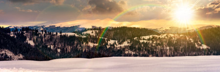 panorama of mountain ridge in winter at sunset. magnificent alpine landscape with snowy peaks with cloudy sky in evening light. storytelling cinematic image under the rainbowの写真素材