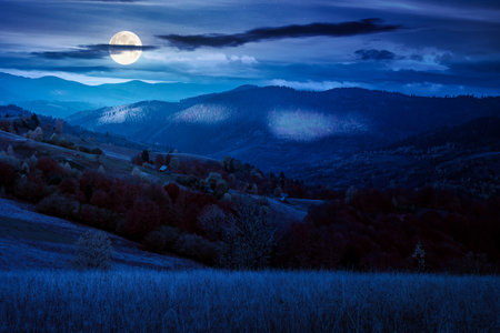 mountain landscape of countryside in autumn at night. mysterious view of range with dappled light on forested slopes in fall foliage in full moon light. place with rolling hillsの写真素材
