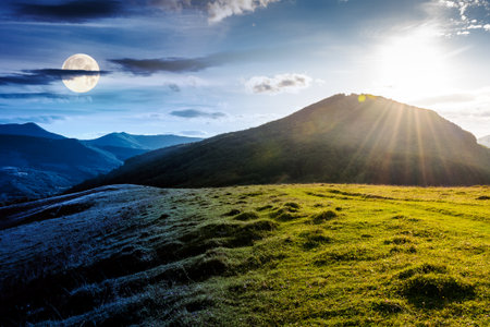 beautiful countryside. day and night time change concept. scenic view of grassy field and rolling hills. wonderful summertime landscape in mountains with sun and moon. transition templateの写真素材