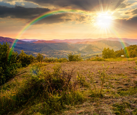 morning landscape of mountains in summer at sunset. rural valley in evening light. beauty of countryside under rainbow. organic hay field green environment concept. stunning place in national parkの写真素材