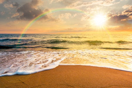 sand beach at the sea for summer vacation concept. beautiful sunset at perfect coast with calm waves and clouds on sky in evening light. scenic landscape for timeless nostalgia book cover with rainbowの写真素材