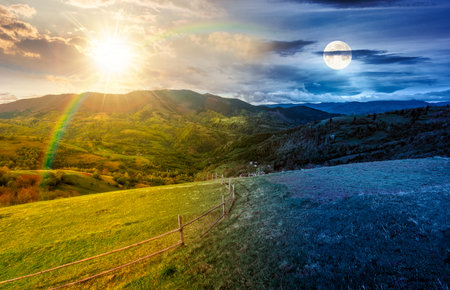 wooden fence on hillside with rural field in mountains. day and night time change concept. scenic countryside landscape with hills and pasture in spring with sun and moon.の写真素材