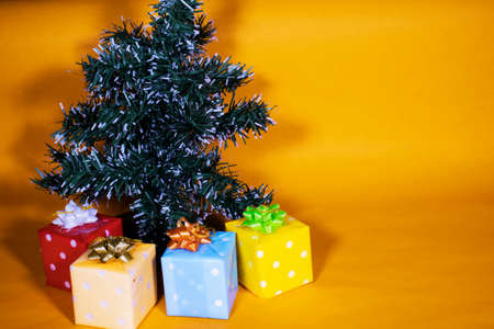 Small green Christmas tree in orange background, with gifts and pine conesの写真素材