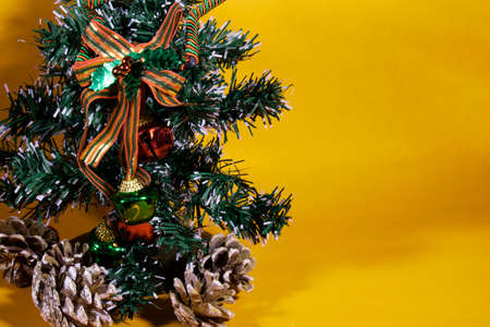Small green Christmas tree in orange background, with gifts and pine conesの写真素材