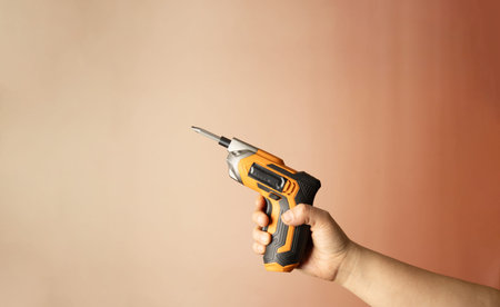 Hand holding cordless screwdriver on pastel background, closeup