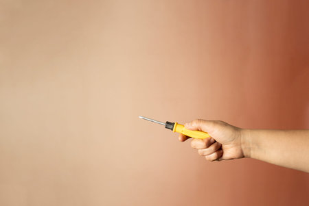 Female hand holding a screwdriver against a pink background with copy spaceの写真素材