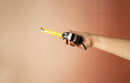 Woman's hand holding a tape measure on a pink wall background.の写真素材