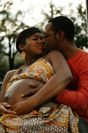 pregnant african american woman kissing with her husband outdoor in a park with tree backgroundの写真素材