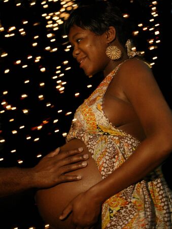 a hand of african american man touching his wife's belly with night bulbs setting on the background. the camera was moved to create moving background lights but the main subject was in focusの写真素材