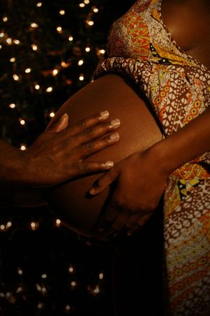 a hand of african american man touching his wife's belly with night bulbs setting on the backgroundの写真素材