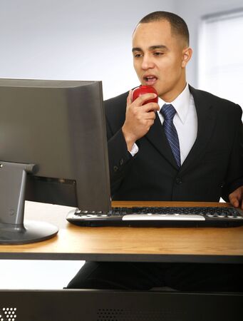 a man eating snack or apple while working in front of his computer in modern office spaceの写真素材