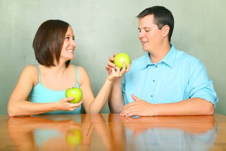 beautiful young female caucasian offering green apple to her boyfriend or husband on kitchen tableの写真素材