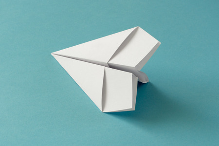 paper origami plane on a blue-turquoise paper backgroundの写真素材
