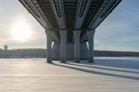 Bridge bottom view in winter. Metal structures and columns against the sky.
