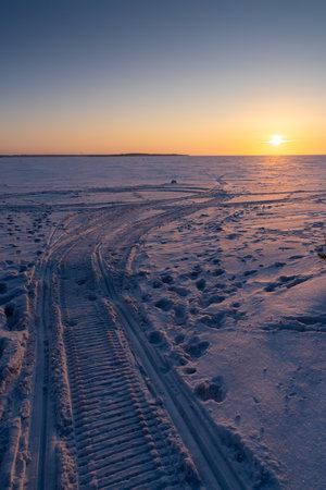 An ice field stretching into the distance with traces of snowmobiles and human tracks.の写真素材