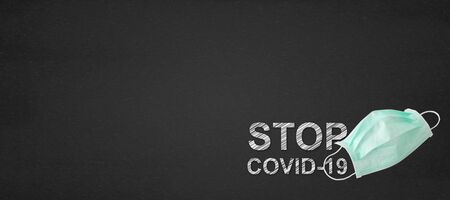 Medical mask with stop covid-19 text on a blackboardの写真素材