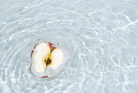 The half of a ripe apple falls in the water.の写真素材