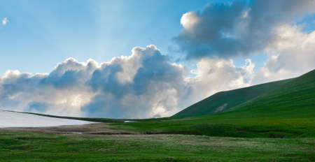 Summer landscape with green grass, mountains and cloudsの写真素材