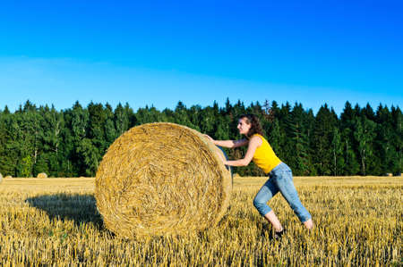 funny girl rolls a haystack in a fieldの写真素材
