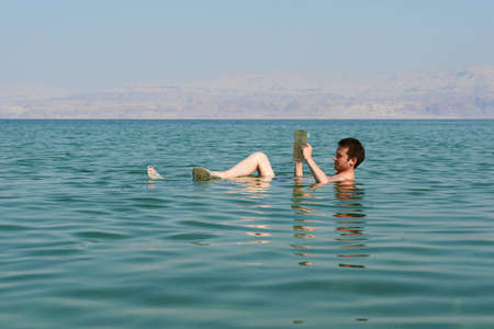 Caucasian man reads a book floating in the waters of the Dead Sea in Israel