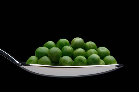 Peas on a spoon over black backgroundの写真素材