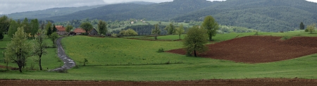 Countryside landscape with village road and arable fields and meadows at mountain valey with hills and clouds in background の写真素材