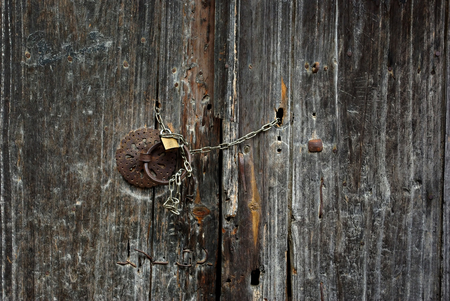 Old wooden gate door locked with padlock and steel chain.の写真素材